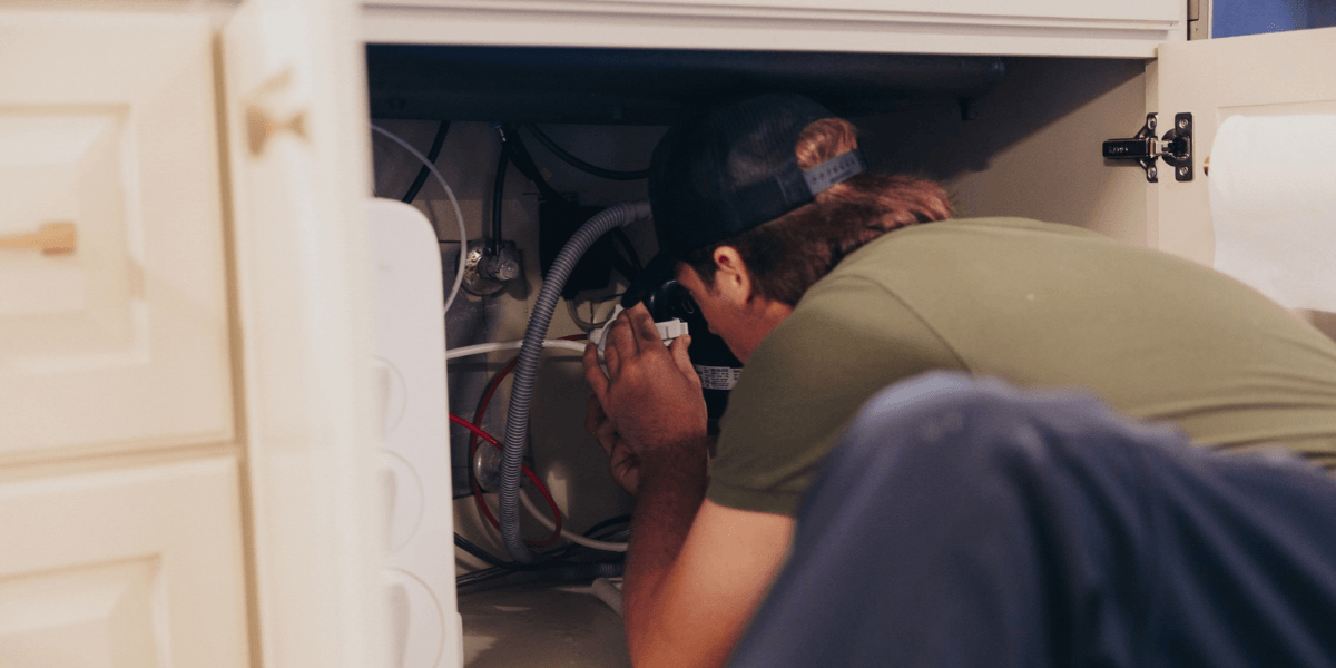 Acadiana Rooter plumber inspecting the drain lines under a kitchen sink to diagnose a clog in a Lafayette, LA home